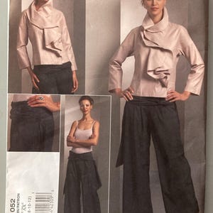 May include: Issey Miyake Vogue Designer Original sewing pattern V1052 for a light pink jacket with a large ruffled collar and wide-leg dark trousers. The pattern envelope displays images of the finished garments in sizes 6, 8, 10, and 12.