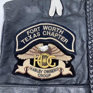 以下が含まれることがあります： FORT WORTH TEXAS CHAPTERおよびHARLEY OWNERS GROUPの文字、鷲のグラフィック、HOGロゴが刺繍された大きなパッチが付いた黒いレザーベスト。ベストの側面には編み込みレザーのトリムがあり、上部には白いパッチが付いています。