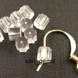 May include: A set of 10 clear plastic earring backs and a gold-toned earring hook. The earring backs are cylindrical and have a textured surface. The earring hook is a simple wire loop.