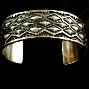 May include: A silver bracelet with a geometric design. The bracelet is made of a thick band of silver with a raised pattern of diamonds.