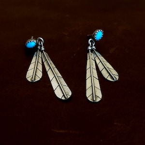 May include: A pair of silver earrings with turquoise stones and feather designs.