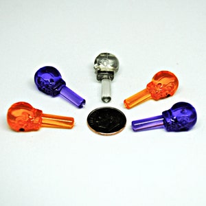 May include: Five miniature skull-shaped Christmas lights, two orange and three purple, with clear plastic stems. A US penny is included for scale.