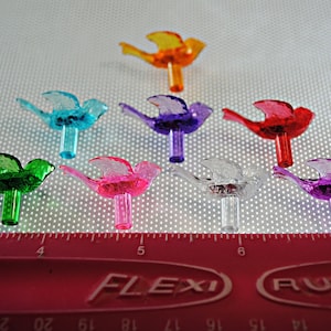 May include: Assortment of eight colorful plastic bird ornaments for a Christmas tree. The birds are in various colors, including red, orange, yellow, green, blue, purple, pink, and clear. The birds are about 2 inches tall and have a small hole at the bottom for hanging.