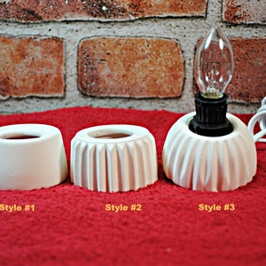 May include: Three white ceramic lamp bases with different styles. The base on the left is a simple cylinder, the middle base has a fluted design, and the base on the right has a fluted design with a bulb and cord.