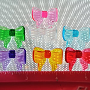 May include: Seven plastic bows in various colors, including pink, green, clear, blue, purple, yellow, and red. The bows are translucent and have a dotted pattern.