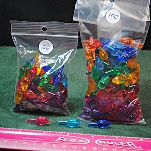 May include: Two bags of colorful plastic Christmas light bulbs. The smaller bag contains 50 bulbs and the larger bag contains 100 bulbs. The bulbs are in a variety of colors, including red, green, blue, orange, and purple.