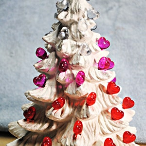 May include: White ceramic Christmas tree with a red star on top and pink and red heart-shaped lights.