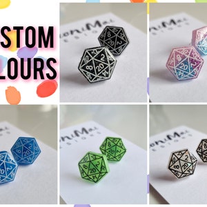 Puede incluir: Un conjunto de seis pares de pendientes de dados d20 de color personalizado. Los dados son negros con números blancos, azules con números blancos, verdes con números blancos, rosas con purpurina azul, blancos con números negros y blancos con purpurina azul.