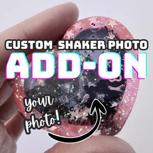 May include: A heart-shaped custom photo shaker add-on with pink glitter and star accents. The text "CUSTOM SHAKER PHOTO ADD-ON" is displayed in white with a blue outline. The words "your photo!" are also visible.