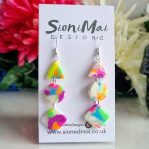 May include: Neon pink, green and blue geometric earrings with a white background. The earrings are made of polymer clay and have a silver hook.