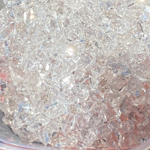 Peut inclure: Une vue rapprochée d'un récipient rempli de cristaux de quartz clairs et facetés. Les cristaux sont de différentes tailles et formes, et ils brillent à la lumière.