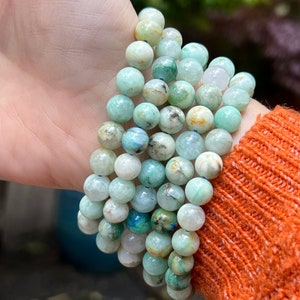 May include: A stack of green, blue, and white gemstone bracelets. The bracelets are made of round beads with a speckled pattern.