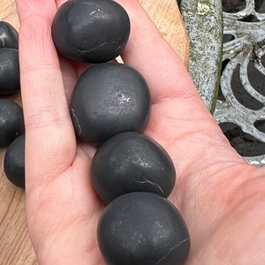 Może przedstawiać: Pięć gładkich, czarnych, okrągłych kamieni, prawdopodobnie obsydianu, ułożonych pionowo w dłoni.