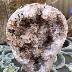 May include: A geode carved into the shape of a skull, with a pink and white exterior and a hollow interior filled with small, clear quartz crystals.