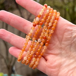 Könnte beinhalten: Eine Strähne orangefarbener Karneolperlen, mit einem Farbverlauf von hellorange bis dunkelorange. Die Perlen sind rund und glatt, und die Strähne ist etwa 45 cm lang.