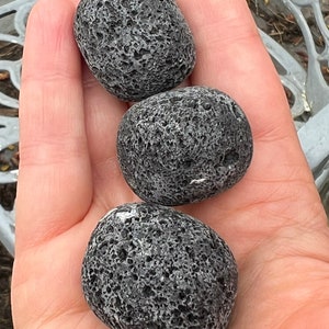 Puede incluir: Tres piedras de lava negras, lisas y redondas, con una textura porosa y moteada.