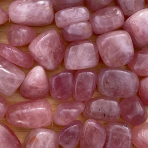 Puede incluir: Una colección de piedras de cuarzo rosa pulidas. Las piedras son de color rosa claro y tienen un acabado liso y pulido.