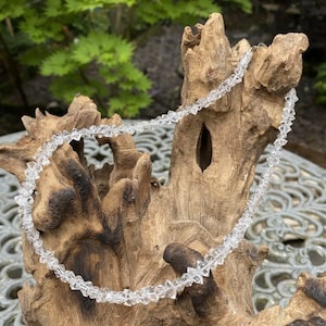 Peut inclure: Un collier en cristal transparent composé de perles facettées. Le collier est présenté sur un morceau de bois flotté.