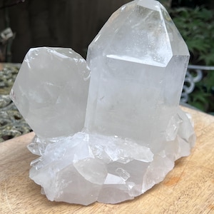Pode incluir: Um aglomerado de cristais de quartzo transparente com duas pontas hexagonais proeminentes orientadas verticalmente que surgem de uma base de formações cristalinas menores e irregulares. O espécime mineral exibe facetas translúcidas.