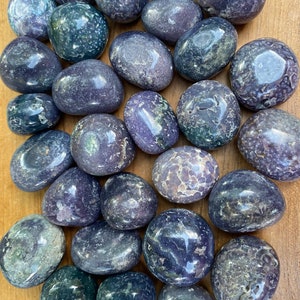 May include: A collection of tumbled purple amethyst stones with a variety of patterns and shades. The stones are smooth and polished, with a natural, earthy look.