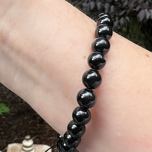 May include: A black beaded bracelet with a simple knot closure. The bracelet is made of round, polished beads.