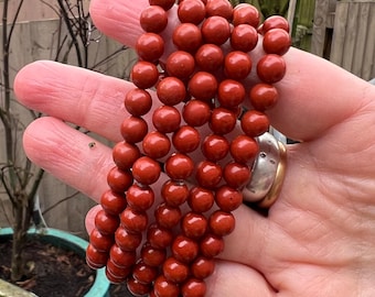 May include: A stack of red gemstone bracelets with round beads. The bracelets are made of red jasper.