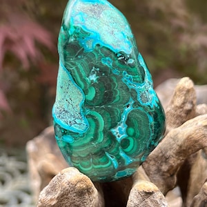 May include: A green and blue malachite gemstone with a swirling pattern. The gemstone is smooth and polished and has a natural, organic shape.