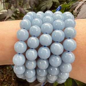 Puede incluir: Una pila de cuentas de piedras preciosas de color azul claro, probablemente de ágata de encaje azul, dispuestas en un patrón circular. Las cuentas son lisas y pulidas, con un brillo sutil.