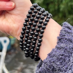 May include: A stack of four black beaded bracelets. The bracelets are made of round, smooth beads.
