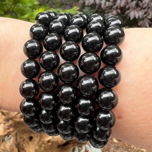 May include: A stack of black beaded bracelets with a high gloss finish. The bracelets are made of round beads and are stacked on a person's wrist.