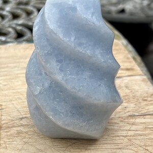 May include: A light blue, carved celestite crystal in a swirl shape. The crystal is smooth and polished.