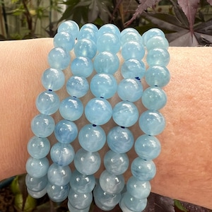 May include: A stack of light blue aquamarine gemstone bracelets with a cloudy, marbled pattern. The bracelets are made with round beads and are strung on elastic.
