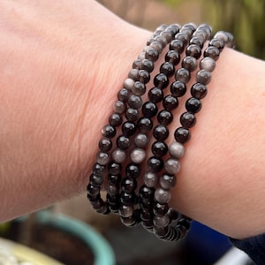 May include: A stack of five bracelets made of black and grey gemstone beads. The bracelets are worn on a person's wrist.