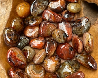 Puede incluir: Una colección de piedras de ágata pulidas con bandas rojas, marrones y blancas. Las piedras son lisas y pulidas, y tienen una variedad de formas y tamaños.