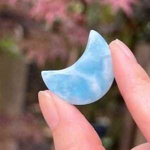 May include: A crescent moon shaped blue aquamarine crystal. The crystal is translucent and has a cloudy appearance.