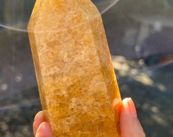 May include: A large, golden yellow citrine crystal point with a smooth, polished surface. The crystal is held in a hand, showcasing its size and shape.