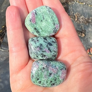 May include: Three green, black and pink tumbled stones. The stones are smooth and polished.