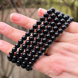 May include: A strand of black onyx beads, strung together to form a bracelet. The beads are round and smooth, and they have a glossy finish.