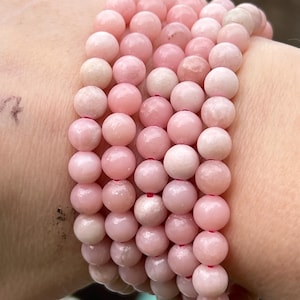 May include: A stack of pink gemstone bracelets with round beads. The bracelets are made of pink opal and have a smooth, polished finish.