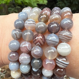 May include: A bracelet made of agate beads. The beads are a mix of gray, white, and brown with swirling patterns.
