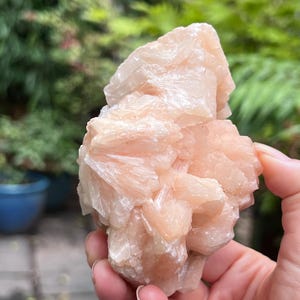 May include: A raw, pale peach-colored mineral specimen featuring a cluster of jagged, crystalline formations with a translucent, multifaceted surface. The stone displays a light, soft orange hue with varying levels of opacity throughout its structure.