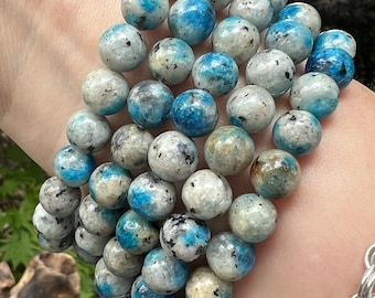 May include: A stack of blue and white beaded bracelets made of kyanite stone. The bracelets are stacked on a person's wrist.