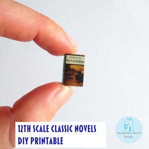 May include: A tiny book, titled "Heart of Darkness" by Joseph Conrad, held up. The cover is brown and beige with a landscape scene. The text at the bottom says "12th Scale Classic Novels DIY Printable".