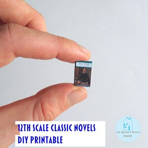 May include: A tiny book titled "Jane Eyre" with a blue cover, held between fingers. The book features a person on the cover. Text at the bottom reads "12th Scale Classic Novels DIY Printable". A logo for "The Wooden Houses Miniatures" is also visible.