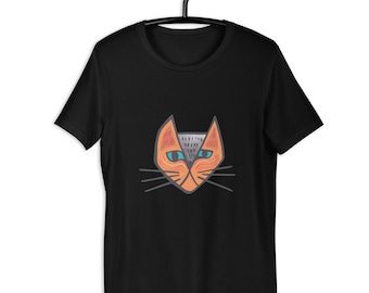 May include: Black t-shirt featuring a stylized orange cat face with blue eyes and gray accents. The cat design has long whiskers and is centered on the shirt. The shirt is hanging on a black hanger.