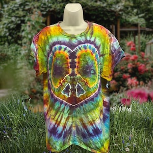 Może przedstawiać: Koszulka tie-dye z motywem znaku pokoju. Koszulka ma kształt serca z symbolem pokoju pośrodku. Kolory to żółty, zielony, fioletowy i niebieski. Koszulka jest prezentowana na manekinie.