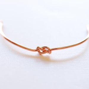 May include: A simple, delicate copper bracelet with a knot design.