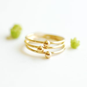 May include: A gold ring with three small, round beads. The ring is stacked on top of itself, creating a layered effect.