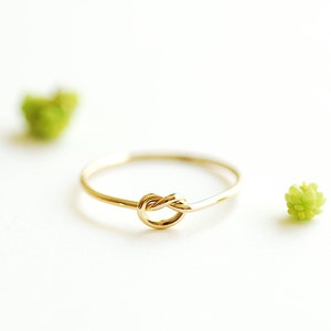 May include: A simple gold ring with a knot design. The ring is on a white background.