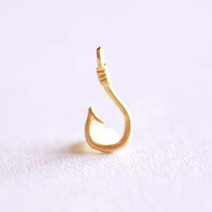 May include: A gold-coloured metal fishing hook charm pendant.